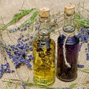 Dos botellas de cristal, una llena de aceite amarillo y la otra de líquido morado, se cierran con tapones de corcho. Se colocan sobre tela de arpillera con ramitas de lavanda seca esparcidas a su alrededor.