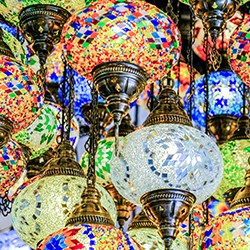 Un grupo de coloridas lámparas turcas con motivos de mosaico y adornos de latón, que cuelgan muy juntas y brillan con una luz vibrante.